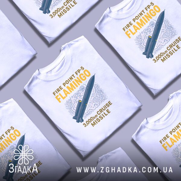 Біла футболка з принтом «Крилата ракета Flamingo», складена на поверхні.