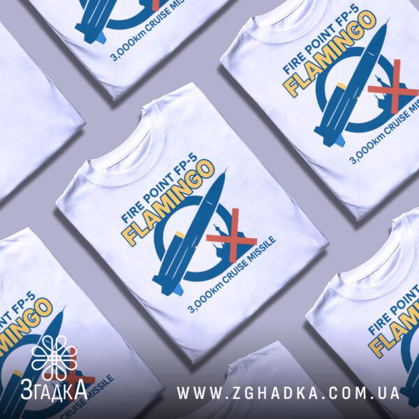Біла футболка з принтом «Крилата ракета Фламінго», складена на поверхні.