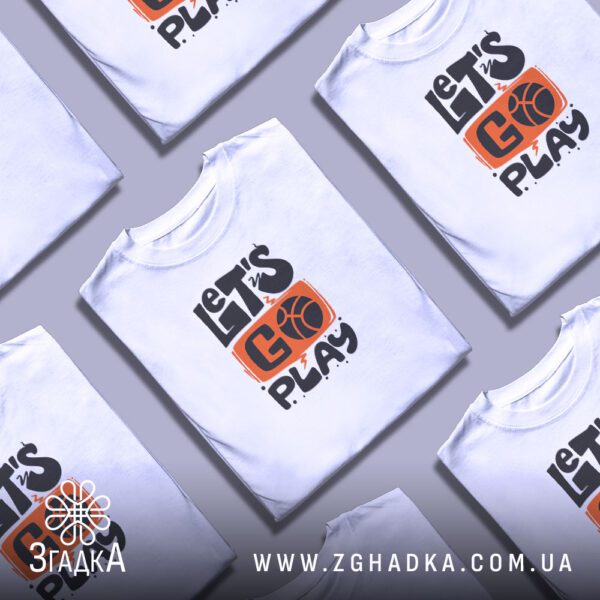 Кілька білих футболок з принтом "let’s go play", складені стопкою або розкладені поруч на світлому фоні.