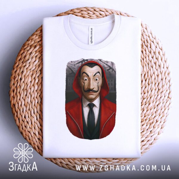 Біла футболка з принтом "маска Далі бунтар", акуратно складена на круглій дерев'яній поверхні.