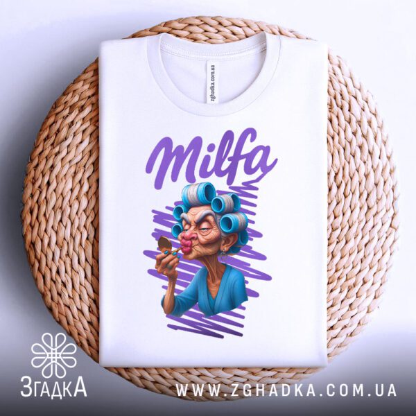Біла футболка з принтом "Milfa кумедний подарунок", складена на світлій поверхні.