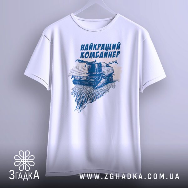 Біла футболка з принтом "найкращий комбайнер подарунок", що висить на вішаку, демонструючи дизайн.