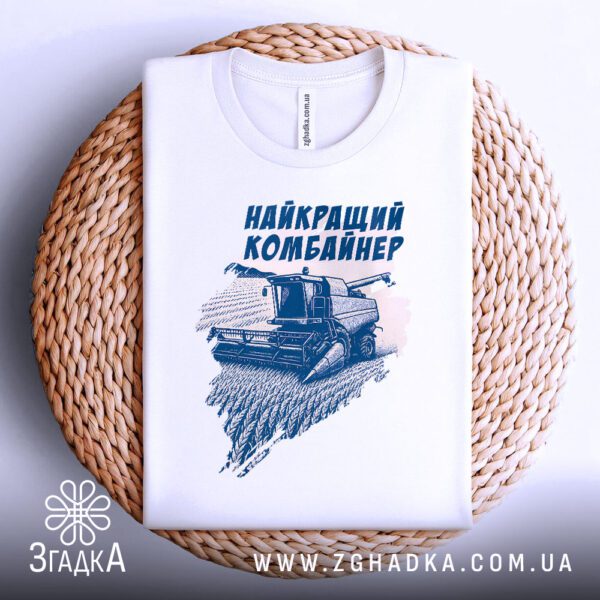 Біла футболка з принтом "найкращий комбайнер подарунок", складена на світлій поверхні.