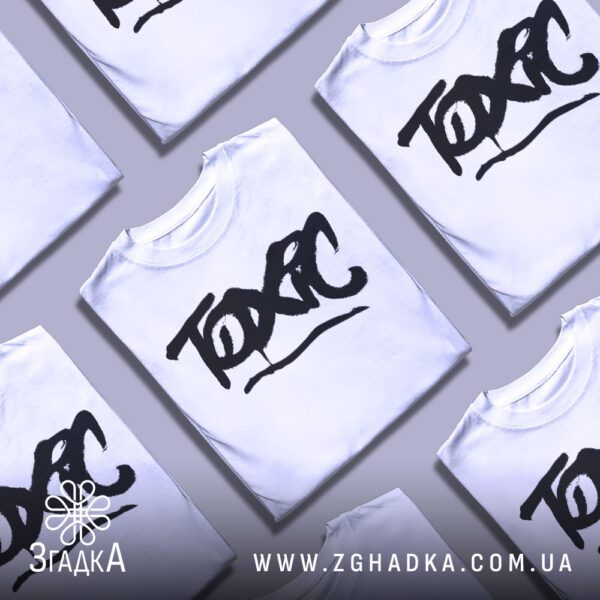 Біла футболка з принтом «Toxic графіті», складена на поверхні.