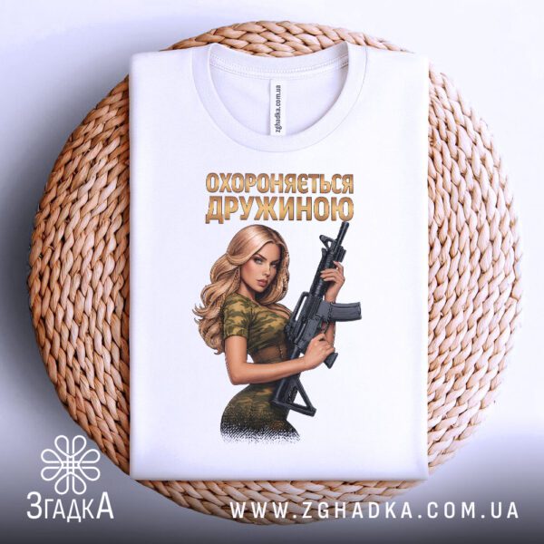 Біла футболка з принтом «Охороняється дружиною» на моделі, демонструючи дизайн.