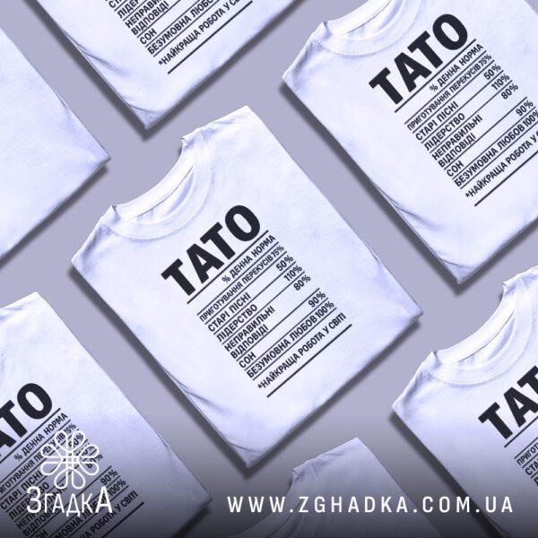 Біла футболка з принтом «подарунок для тата», складена на поверхні.