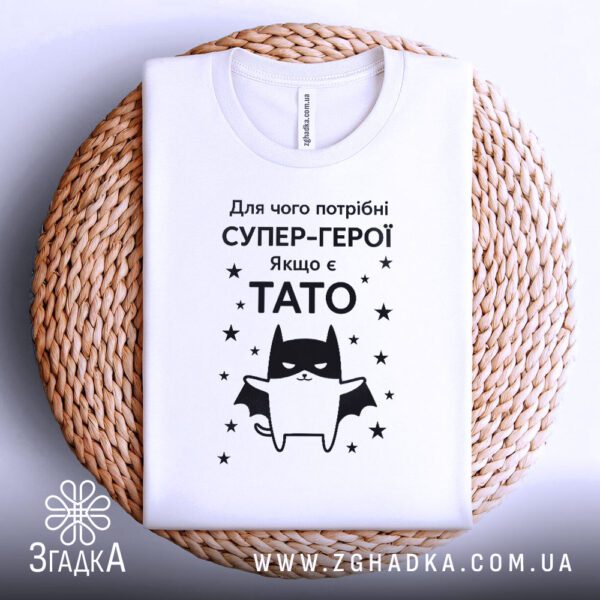 Біла футболка з принтом Подарунок для тата, що висить на вішаку.