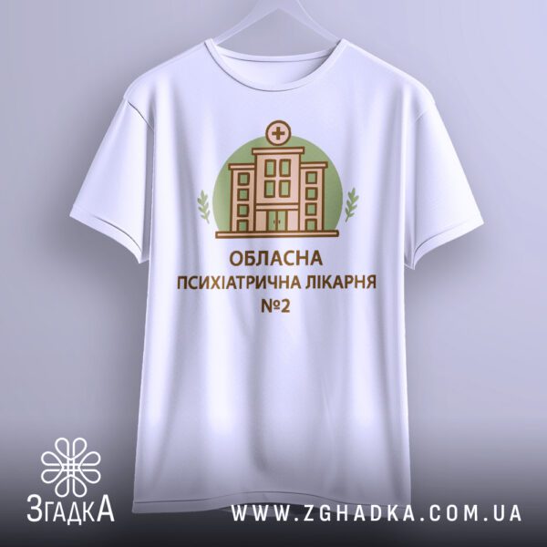 Біла футболка з принтом "психіатрична лікарня", що висить на вішаку, демонструючи дизайн.