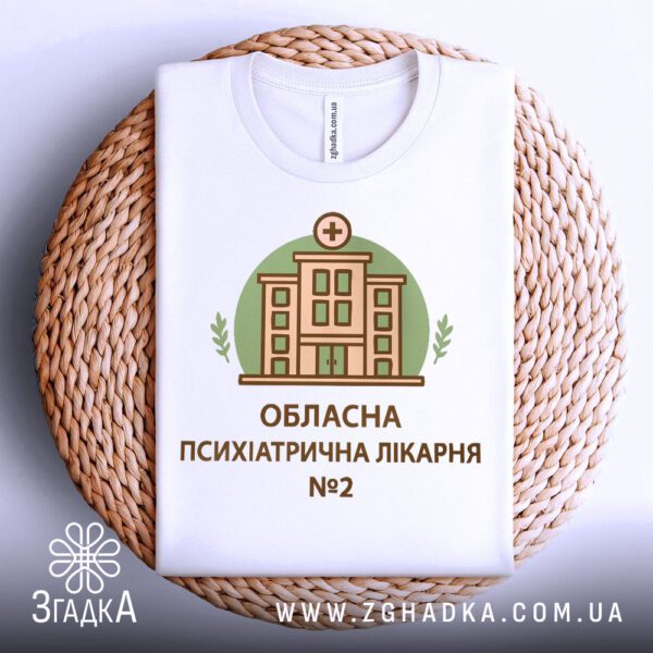 Біла футболка з принтом "психіатрична лікарня", складена на світлій поверхні.