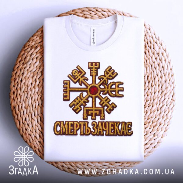 Біла футболка з принтом «Смерть зачекає», що висить на вішаку.