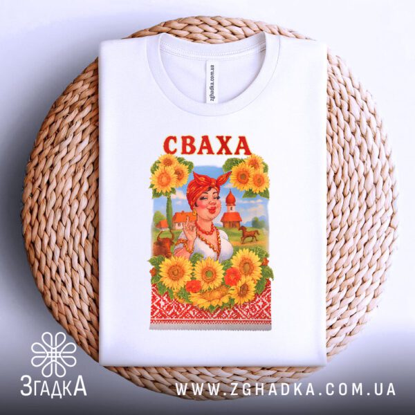 Біла футболка з принтом "Сваха на подарунок", складена на світлій поверхні.