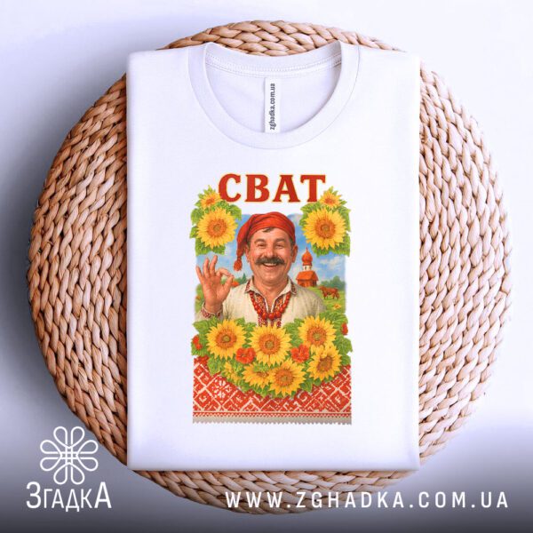 Біла футболка з принтом "Сват на подарунок", складена на світлій поверхні.