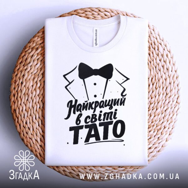 Біла футболка з принтом «тато приклад сили», що висить на вішаку.