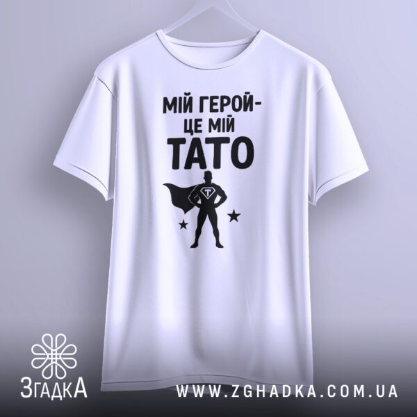 Біла футболка з принтом «тато завжди герой» на моделі.