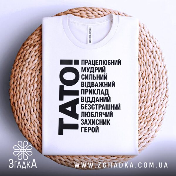 Біла футболка з принтом «тато завжди поруч», що висить на вішаку.