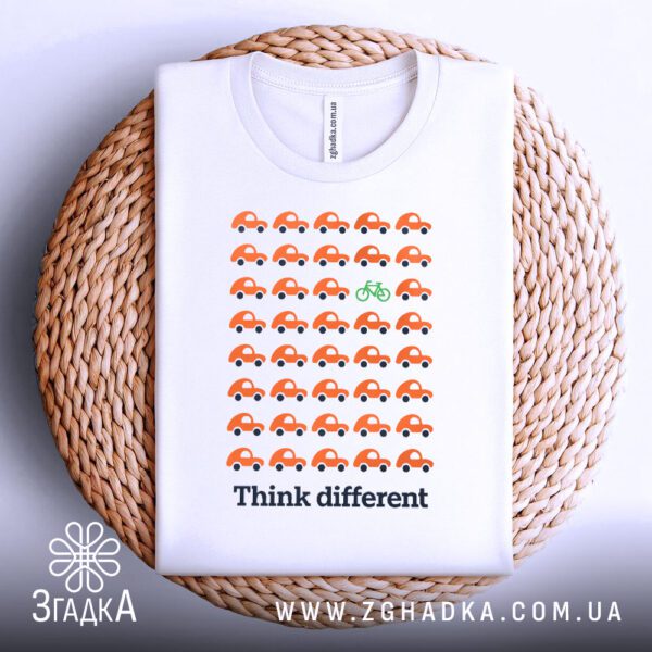Біла футболка з принтом "think different стиль", акуратно складена на круглій дерев'яній поверхні.