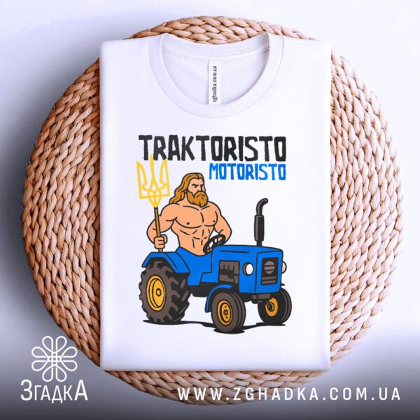 Біла футболка з принтом "трактористо мотористо Україна", складена на світлій поверхні.