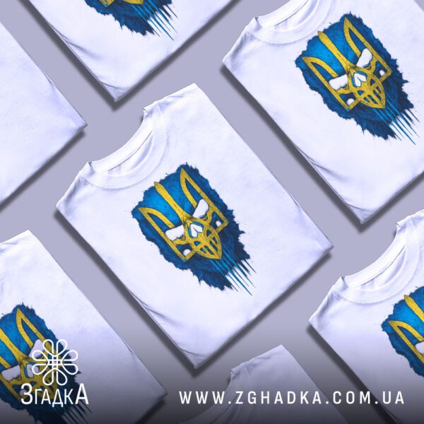 Біла футболка з принтом «Тризуб синьо жовтий», складена на поверхні.