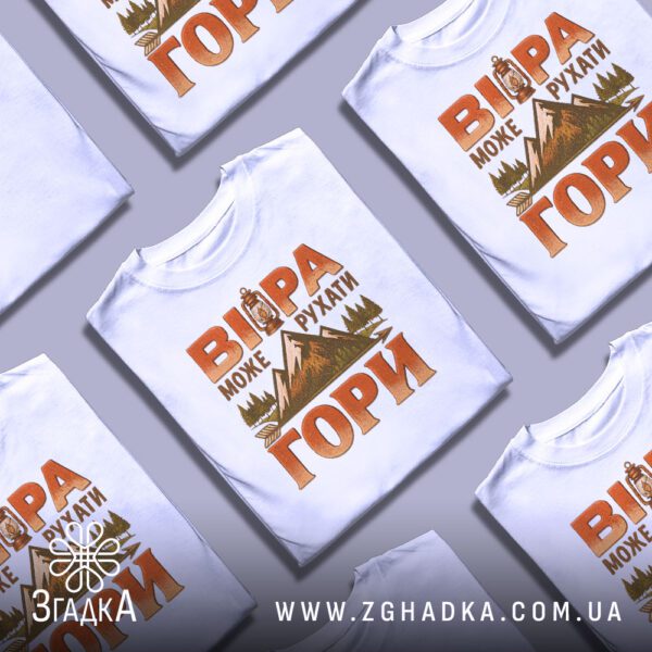 Біла футболка з принтом «віра рухає гори», складена на поверхні.