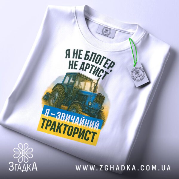 Крупний план принту "я звичайний тракторист" на білій футболці, що детально показує ілюстрацію.