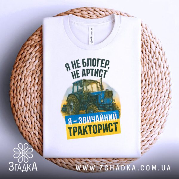 Біла футболка з принтом "я звичайний тракторист", складена на світлій поверхні.