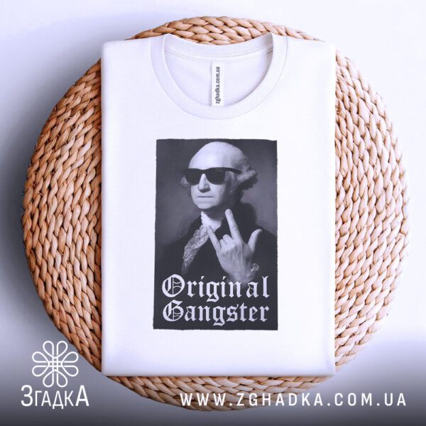 Біла футболка з принтом "з написом Gangster", акуратно складена на круглій дерев'яній поверхні.