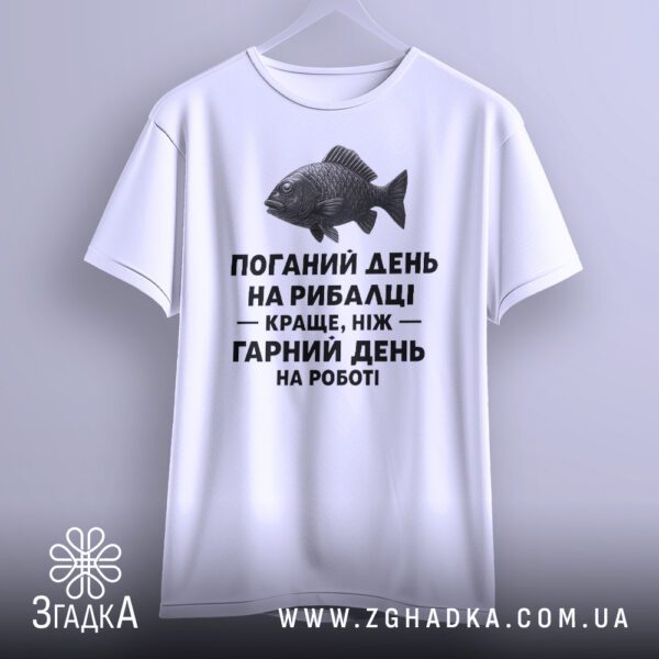 Біла футболка з написом "з написом рибалка", що висить на вішаку, демонструючи дизайн.