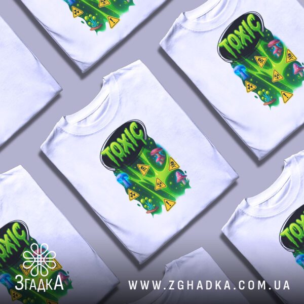 Біла футболка з принтом «Toxic», складена на поверхні.