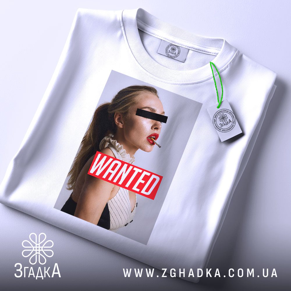 Складена біла футболка з принтом "з написом Wanted" та етикеткою "Згадка".