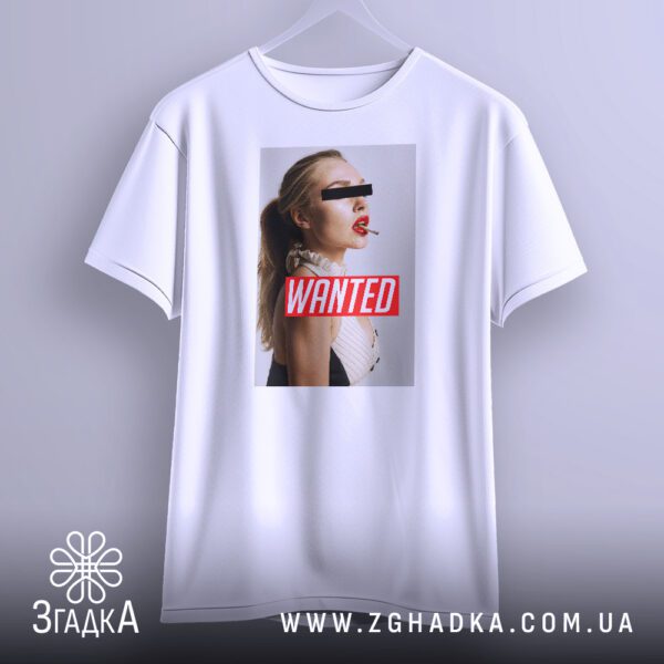 Біла футболка з принтом "з написом Wanted", що висить на білих плічках, демонструючи дизайн.