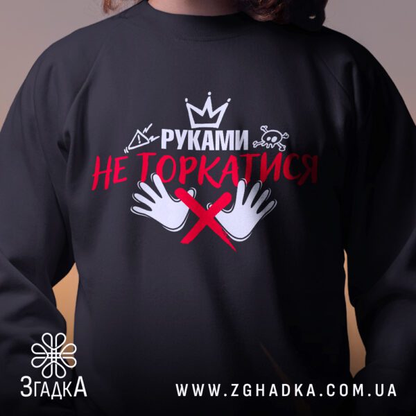 Крупний план принту "руками не торкатись" на чорному світшоті, що детально показує ілюстрацію.
