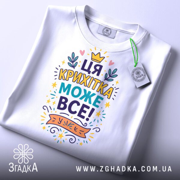 Біла футболка з написом "Ця крихітка може все!", вид спереду.