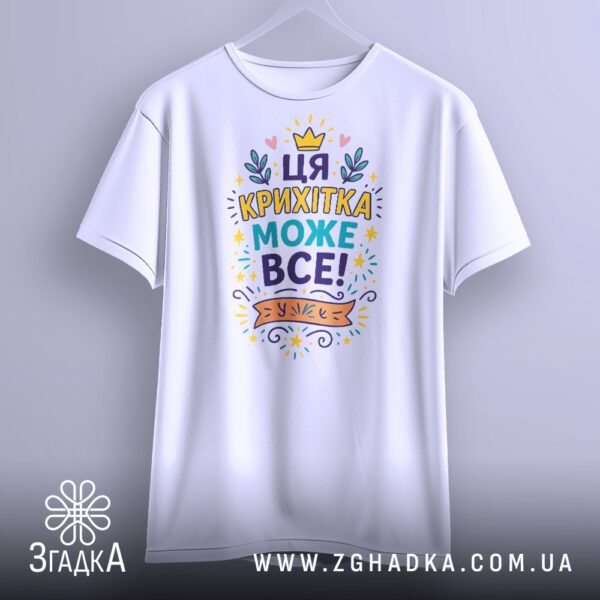 Біла футболка з написом "Ця крихітка може все!", крупний план.