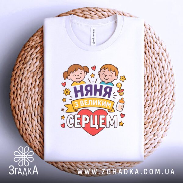 Футболка няня з серцем акуратно складена на плетеній підкладці, виглядає як подарунок.