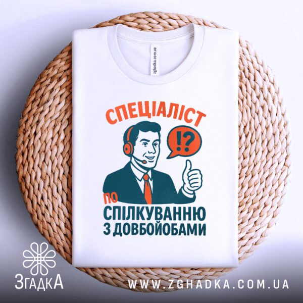 Біла футболка з принтом "Спеціаліст по спілкуванню з довбойобами", складена.