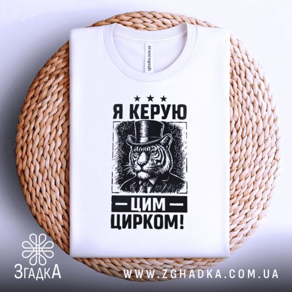 Біла футболка з принтом "Я керую цирком", складена.