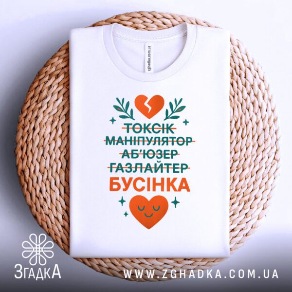Біла футболка з принтом "Я не токсік...Бусінка", складена.