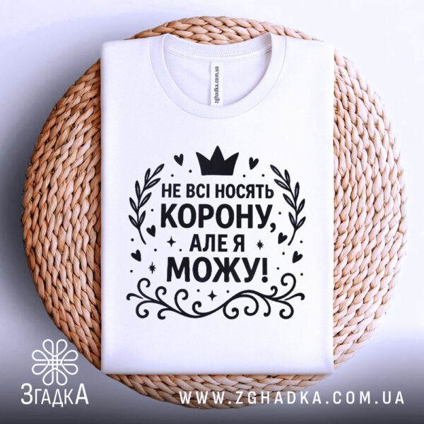 Біла жіноча футболка з принтом "Не всі носять корону", складена.