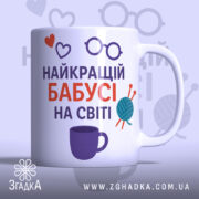 Чашка бабусі день народження. Чашка білого кольору з принтом, що містить напис 'НАЙКРАЩИЙ БАБУСІ НА СВІТІ' у червоному та фіолетовому кольорах, а також ілюстрації у вигляді сердець, окулярів та клубка пряжі. Ручка чашки з класичним дизайном, край рівний, поверхня глянцева. Фон світло-фіолетовий з малюнками окулярів.