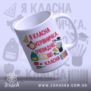Чашка для класного керівника, біла, з яскравим принтом на передній частині, що містить текст червоного кольору та ілюстрації шкільних предметів. Ручка класичної форми, край рівний, поверхня глянцева. Чашка нахилена, фон з легкими елементами шкільної тематики.