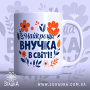 Чашка найкраща внучка подарунок. Чашка білого кольору з яскравим принтом, на якому зображені червоні та помаранчеві квіти, а також текст синього кольору. Ручка круглої форми, край рівний, поверхня глянцева. Фон ніжно-фіолетовий з абстрактними квітковими елементами.