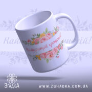 Чашка найкращій хрещеній подарунок. Чашка білого кольору з глянцевою поверхнею, з квітковим принтом і написом 'Найкращій хрещеній!' на передній частині. Ручка стандартної форми, край рівний, фон ніжно-фіолетовий.