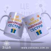 Чашка найкращої сестри подарунок, дві білих чашки з кольоровим принтом, зображення з легким нахилом, фон світло-фіолетовий, на чашках напис великими літерами: 'ЦЕ ЧАШКА НАЙКРАЩОЇ СЕСТРИ', з квітами та подарунком, ручки круглі, краї рівні, глянцева поверхня.