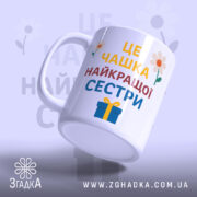 Чашка найкращої сестри подарунок, біла з кольоровим принтом, зображення з легким нахилом, фон світло-фіолетовий, на чашці напис великими літерами: 'ЦЕ ЧАШКА НАЙКРАЩОЇ СЕСТРИ', з квітами та подарунком, ручка кругла, край рівний, глянцева поверхня.