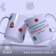 Чашка новорічна для хрещеного, біла з яскравими малюнками, показана з бокового ракурсу, фон світло-фіолетовий, на чашці зображення новорічних елементів та напис: 'новорічне горнятко найкращого хрещеного на світі', ручка стандартна, край рівний, глянцева поверхня.