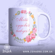 Чашка подарунок для бабусі, біла з ніжним квітковим принтом, ракурс з боку, фон світло-фіолетовий, напис червоним шрифтом "Мій чудовий бабусі!", ручка округлої форми, край гладкий, глянцевий.