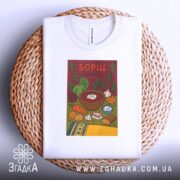 Футболка борщ українська кулінарія, біла, складена на круглому кошику, фон світло-сірий, принт з малюнком борщу та інгредієнтів, кольори яскраві, текст "БОРЩ" на червоному фоні.