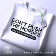 Футболка don't push the horses, біла, складена на поверхні, з видимим етикеткою, фон світло-сірий, принт чорного кольору з текстом "DON'T PUSH THE HORSES" та українським перекладом "НЕ ЖЕНИ КОНЕЙ".