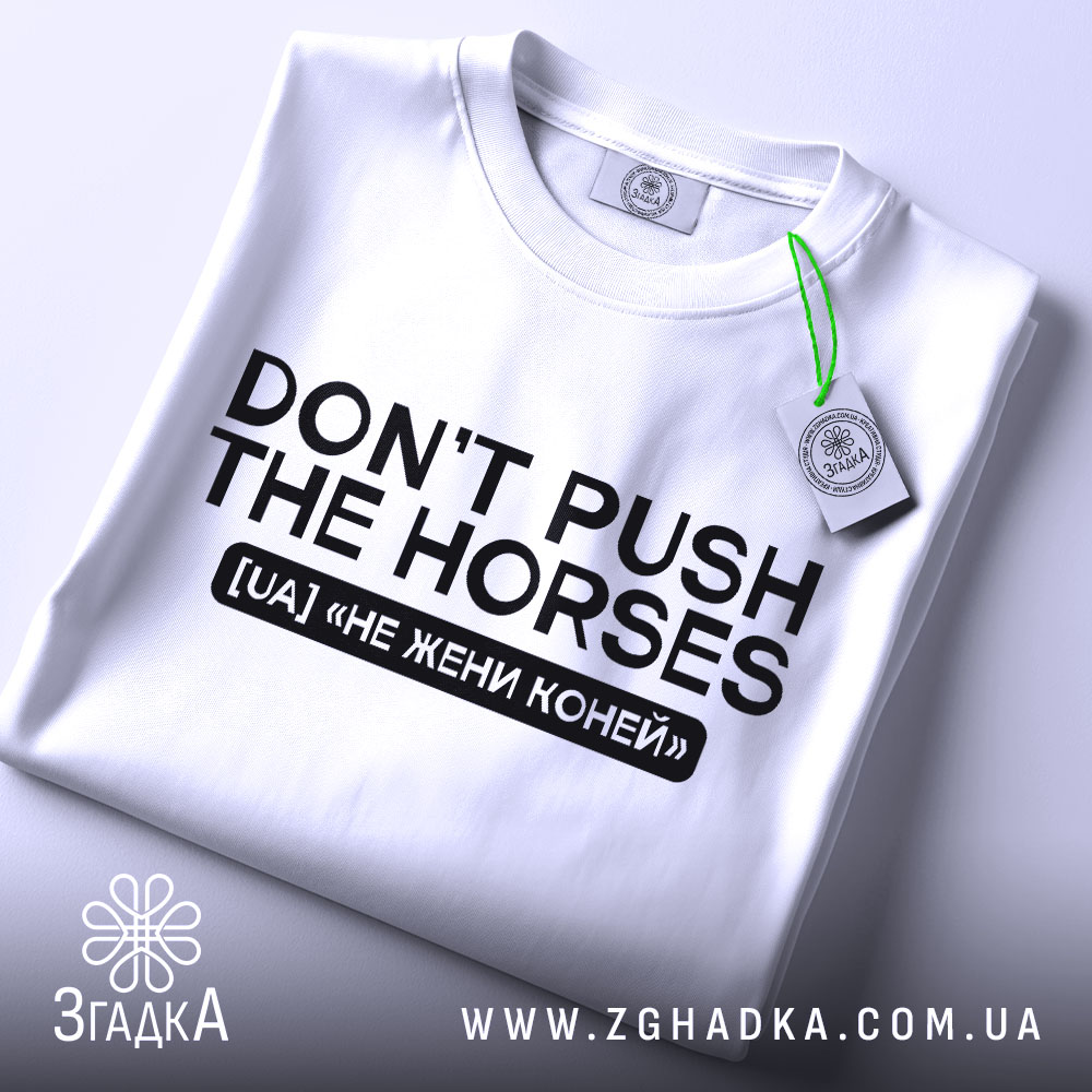 Футболка don't push the horses, біла, складена на поверхні, з видимим етикеткою, фон світло-сірий, принт чорного кольору з текстом "DON'T PUSH THE HORSES" та українським перекладом "НЕ ЖЕНИ КОНЕЙ".