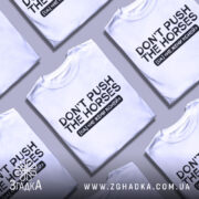 Футболка don't push the horses, біла, розкладена на поверхні, фон світло-сірий, кілька футболок в одному кадрі, принт чорного кольору з текстом "DON'T PUSH THE HORSES" та українським перекладом "НЕ ЖЕНИ КОНЕЙ".
